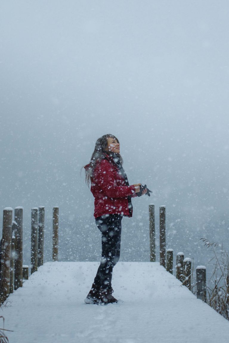 Profilfoto der Fotografin, die auf einem verschneiten Steg steht, nach oben schaut und den Schnee beobachtet